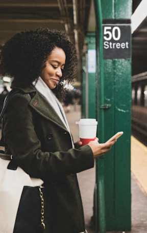 A woman is standing on a subway platform with a coffee cup in her hand at The Ellington Apartments, New York, NY, 10019