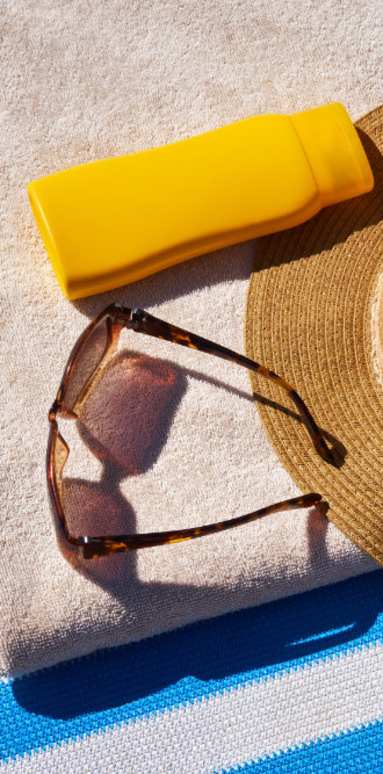 A straw hat, sunglasses, and sunscreen are placed on a towel.