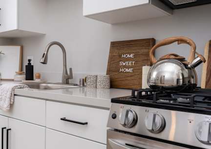 A modern kitchen with a stove, sink, and a sign that says "Home Sweet Home".
