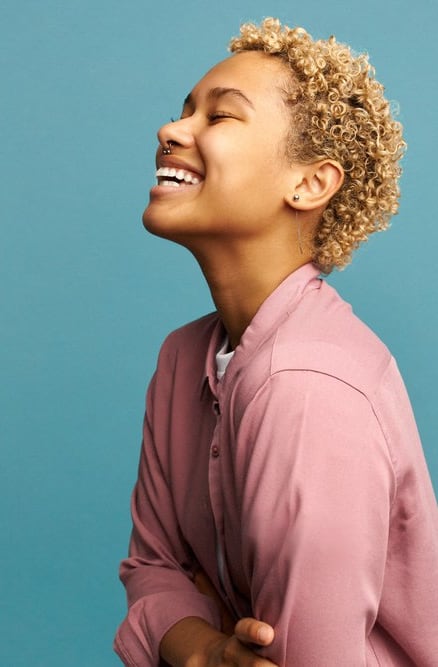 a woman laughing while wearing a pink shirt and a blue background
