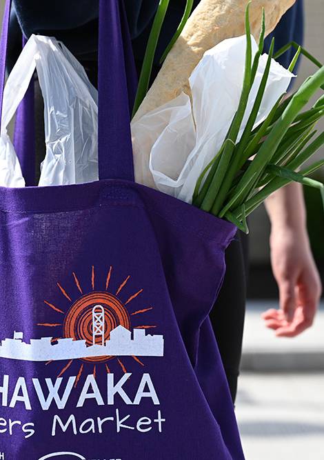 A person is carrying a purple tote bag with the logo of Mishawaka Farmers Market.