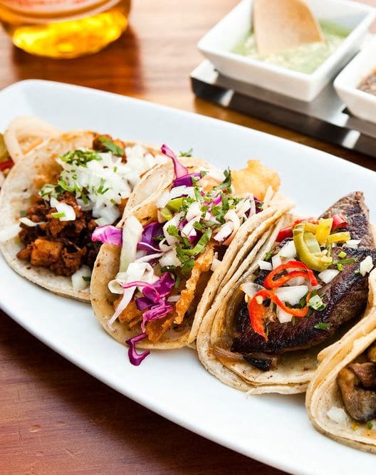 four tacos on a white plate on a wooden table