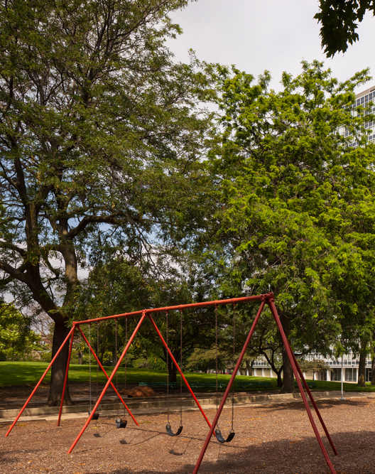 A playground with swings and a slide is in the foreground with a tall building in the background.