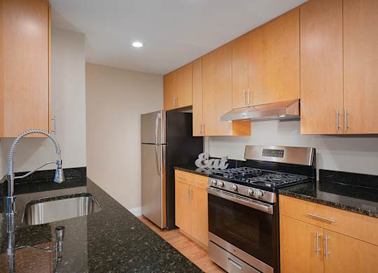 Kitchen with black granite countertops, stainless steel refrigerator and stove. Shows upper and lower oak colored cabinets.