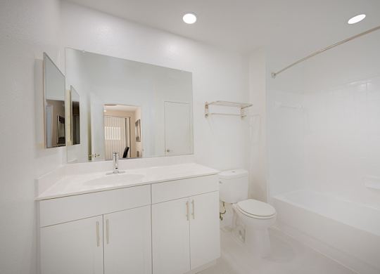 A full bathroom with tub shower, white cabinets, white ceramic tile flooring, large mirror.