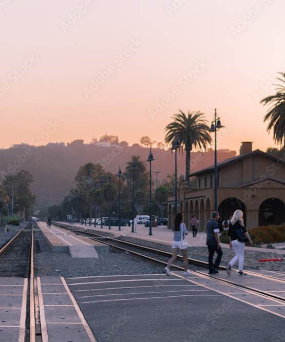 Two people are walking on the street near the train tracks.