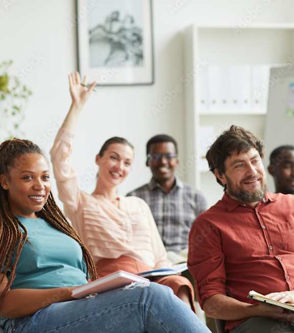 A group of people are sitting in a room with one person raising their hand.