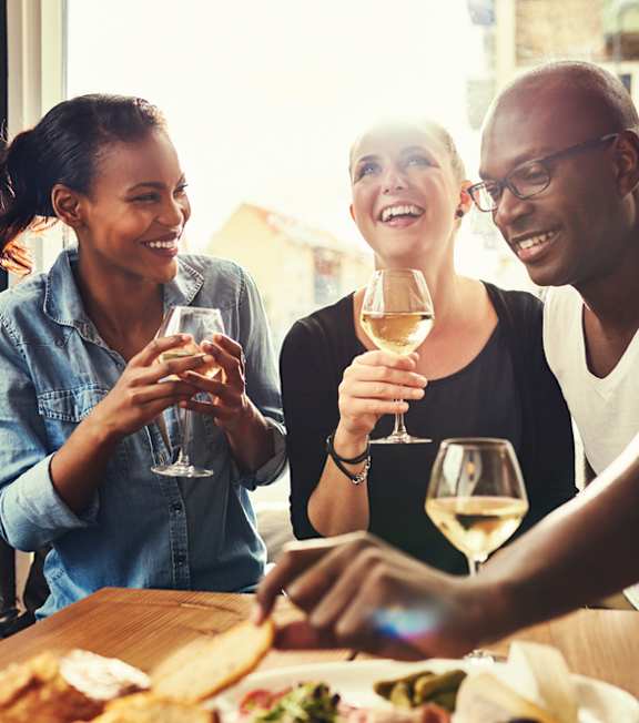three people drinking wine and eating at a restaurant