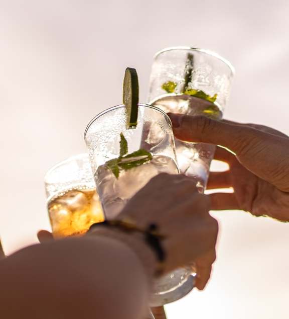 Two hands holding glasses of a drink with a garnish.