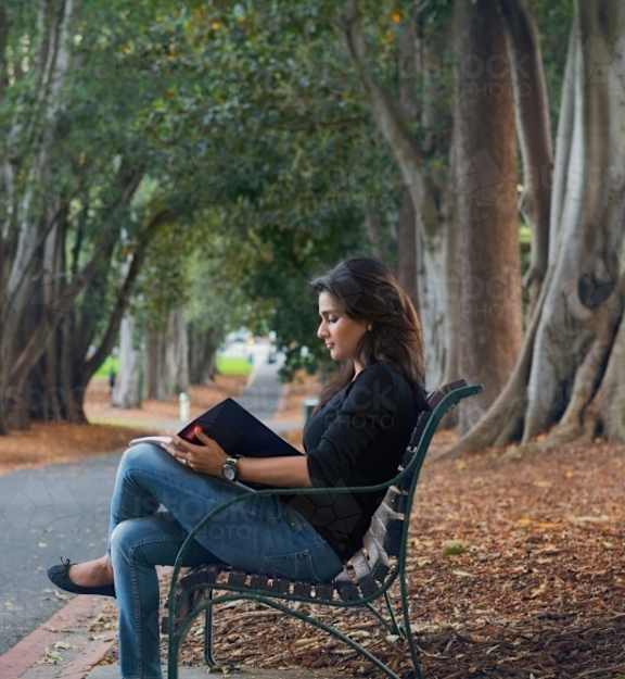 a woman sitting on a park bench reading a book