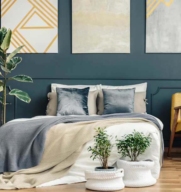 A bedroom with a bed, chair, and potted plants.