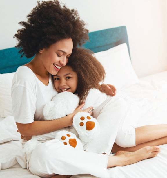 a mother and daughter sitting on a bed with a teddy bear