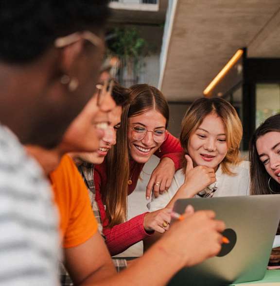 A group of people are gathered around a laptop, looking at it intently.