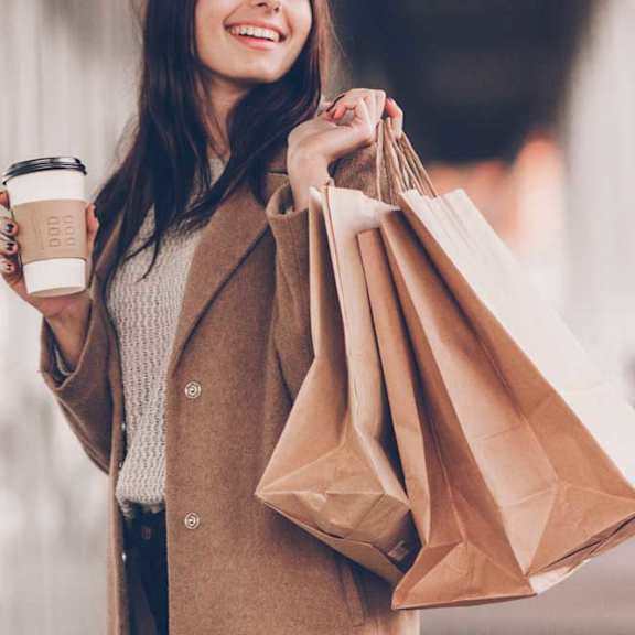 A woman is holding a cup of coffee and shopping bags.