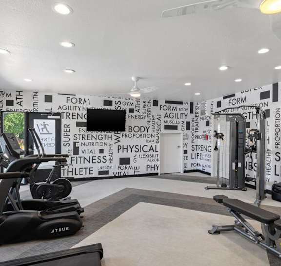 A gym with a treadmill, bench and a wall of fitness related words.