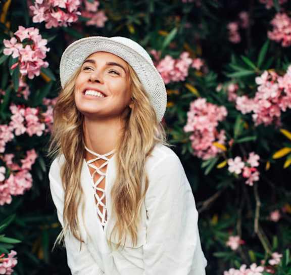 A woman in a white dress and hat is standing in front of pink flowers.at London Terrace Gardens, New York New York