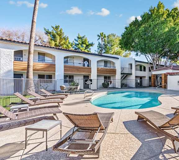 A pool surrounded by chairs and trees in front of a building.