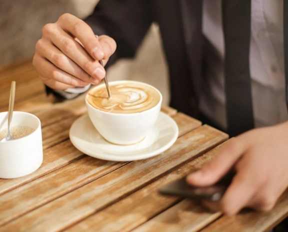 A person is sitting at a table with a cup of coffee and a small container of sugar.