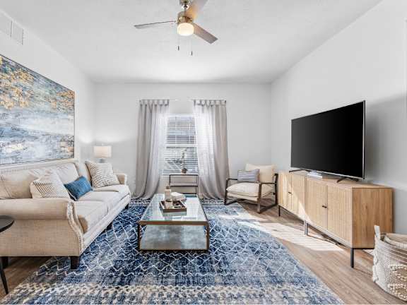 A living room with a beige couch, a coffee table, a television, and a painting on the wall.