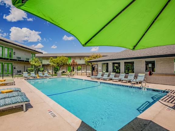 Fusion Las Vegas pool with green umbrella, patterned lounge chairs, and buildings surrounding.