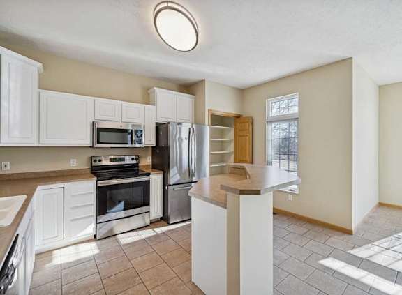 A kitchen with white cabinets and a stainless-steel fridge.