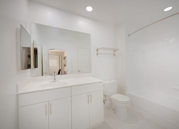 A full bathroom with tub shower, white cabinets, white ceramic tile flooring, large mirror.