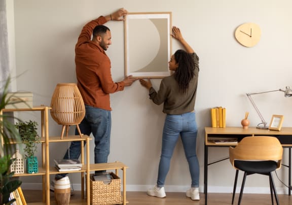 a man and a woman are hanging a mirror on a wall