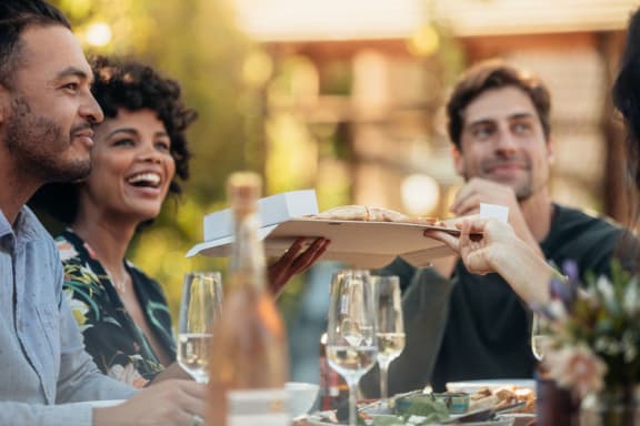 a group of people sitting around a table eating pizza and drinking wine at The Willard Apartments, Maryland, 21117