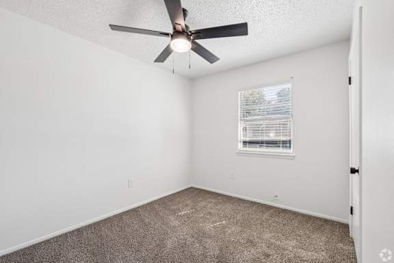 A room with a ceiling fan and a window with blinds.
