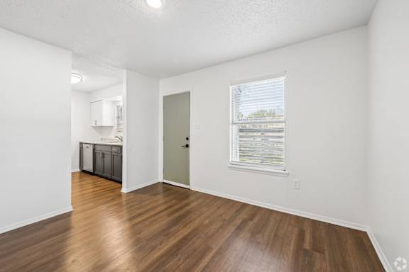 A room with a wooden floor and a window showing a view of trees and a building.