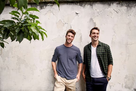 two men standing next to each other in front of a white wall