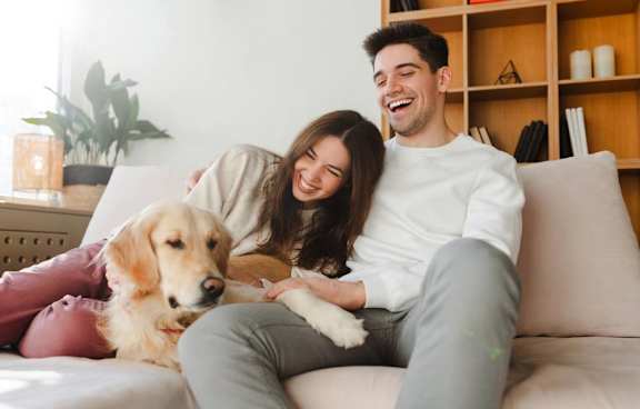 A man and woman are sitting on a couch with a dog between them.
