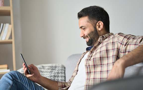 A man in a plaid shirt is sitting on a couch using a smartphone.