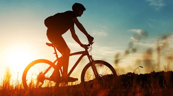  Man bikes rugged trail in golden sunlight near apartments.