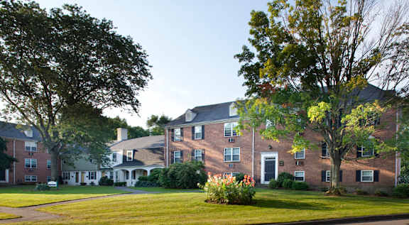 A tall apartment building with balconies and trees in the foreground.
