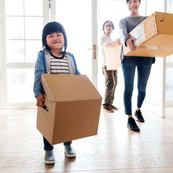 a young girl holding a cardboard box while others carry boxes in a room