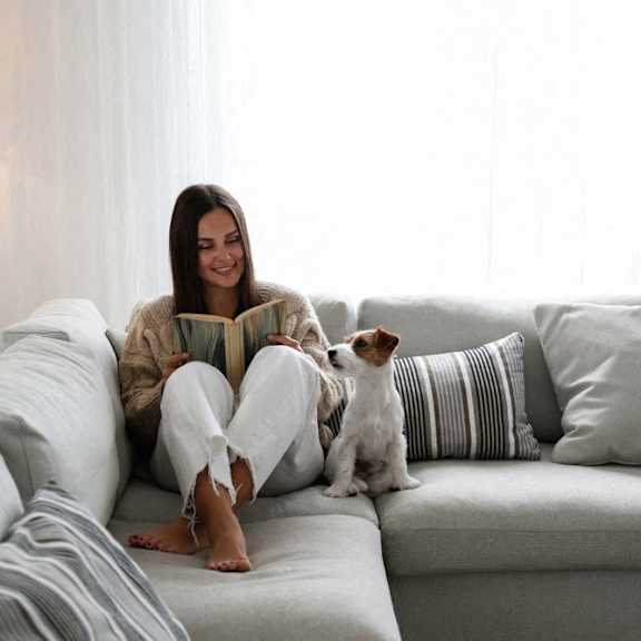 a woman sitting on a couch reading a book with her dog
