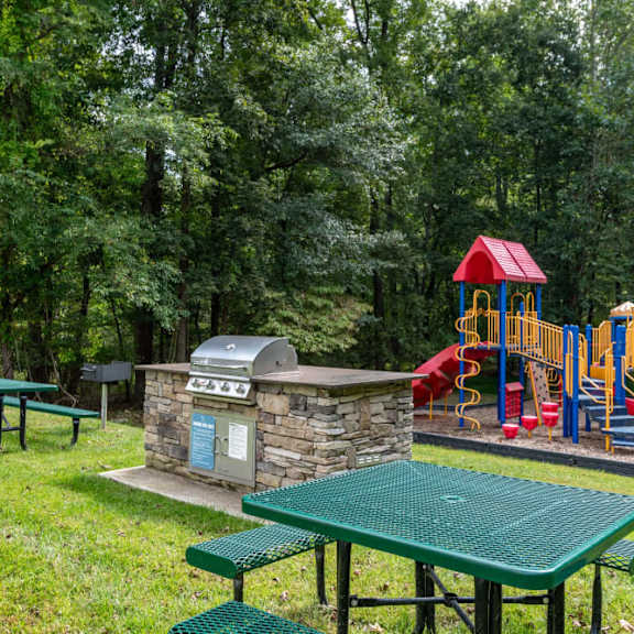 A playground with a slide, swings, and a picnic table is surrounded by trees.