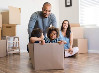 A family of three is sitting in a cardboard box in their new home.