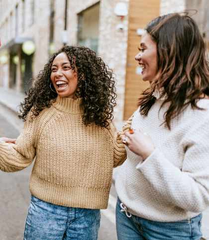 three women walking down the street laughing and holding hands