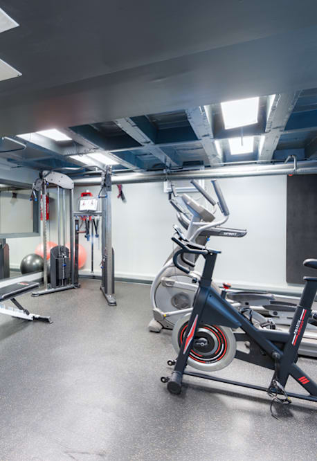 A gym with a variety of equipment including a stationary bike, dumbbells, and a television.