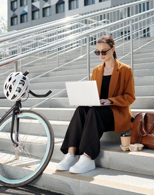 a woman sitting on the steps with a bike using a laptop
