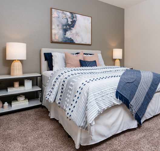 A bedroom with a large bed and a nightstand with a lamp. at Miro at the Parc Apartments, Henderson , NV, 89074