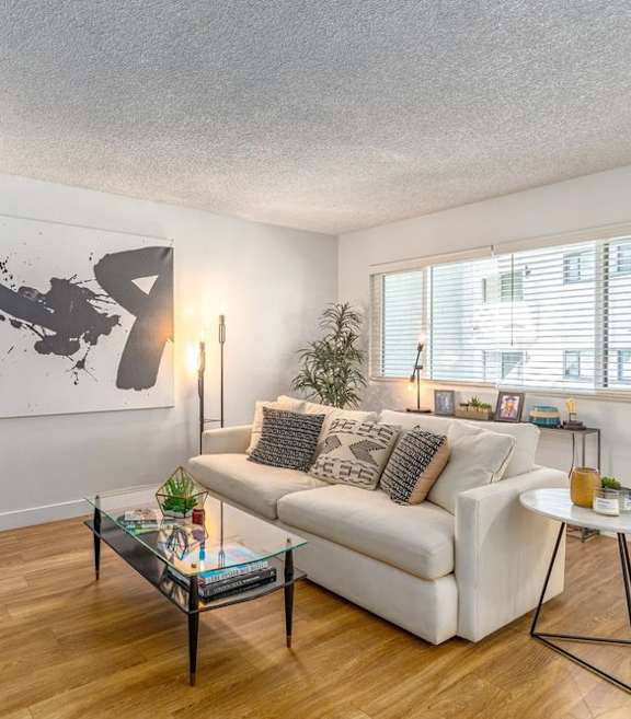 A living room with a white couch, a coffee table, and a large abstract painting on the wall.