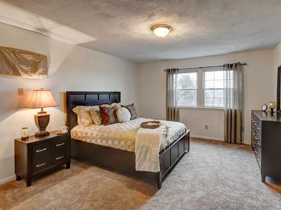 A bedroom with a large bed and a nightstand with a lamp at Kings Gate West Apartments, Camillus, NY