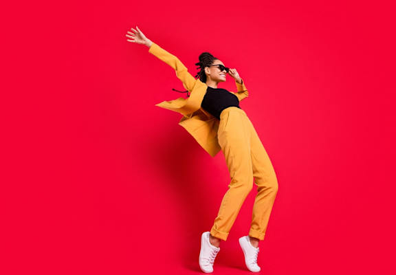 a woman in a yellow suit and sunglasses dancing in front of a red background
