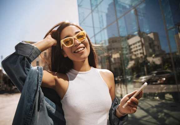a woman holding a cell phone and wearing yellow sunglasses