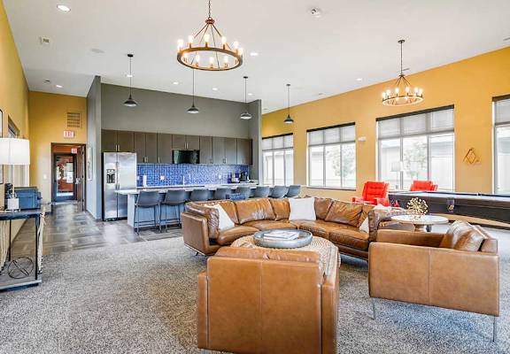 A clubhouse kitchen with large island and several bar stools, and a lounge area with a leather couch, chairs, and a pool table.