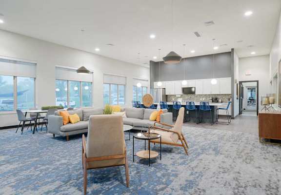 Clubhouse and resident lounge with modern seating, blue accent carpeting, and an open layout connected to the community kitchen.