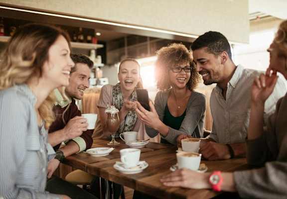 a group of people sitting around a table laughing and looking at a cell phone